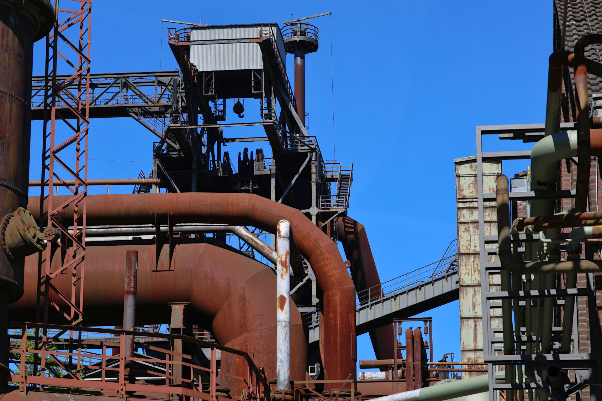 Industrial structures, pipes and machinery beneath a clear blue sky.