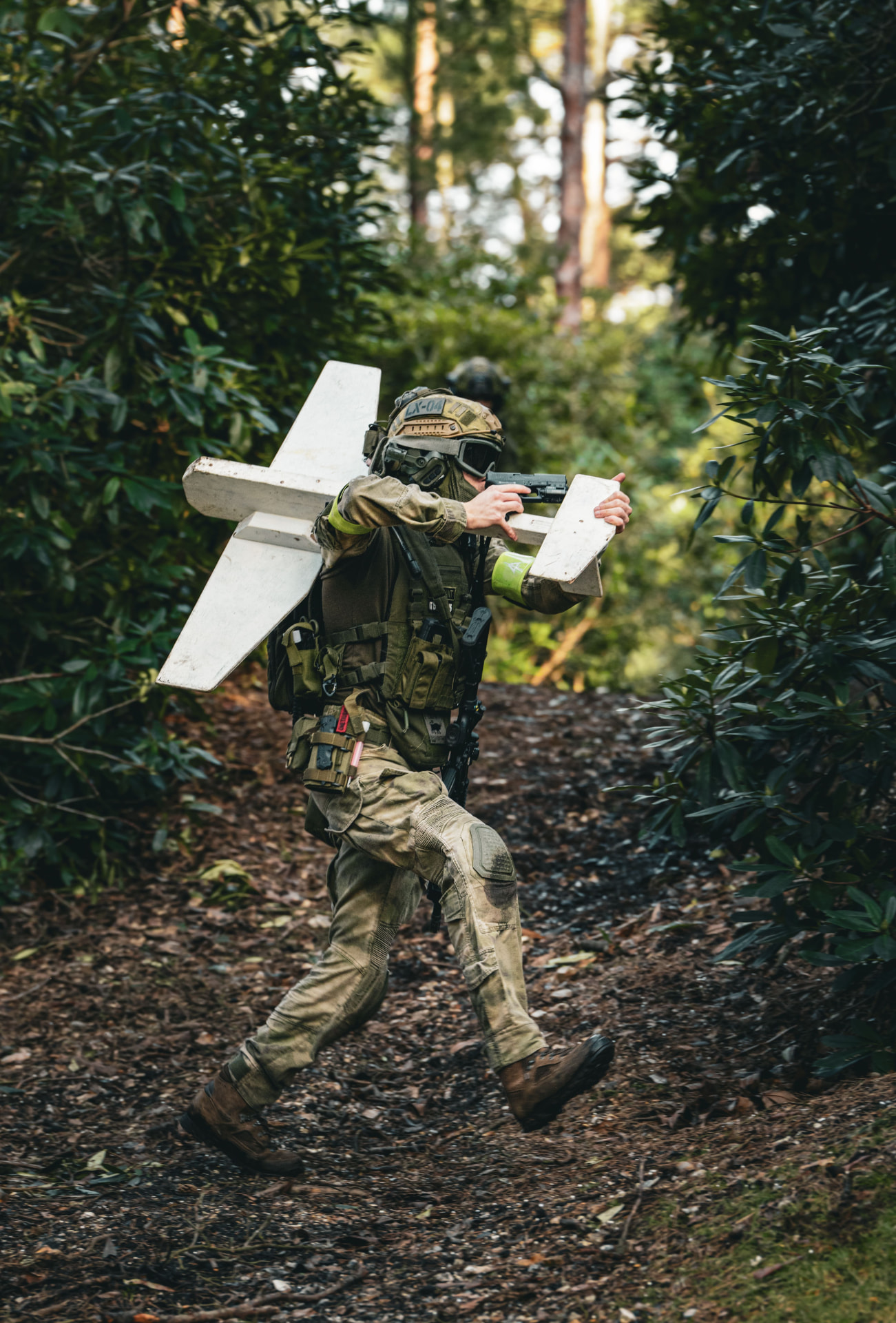 A soldier carrying a fixed-wing drone through woodland.